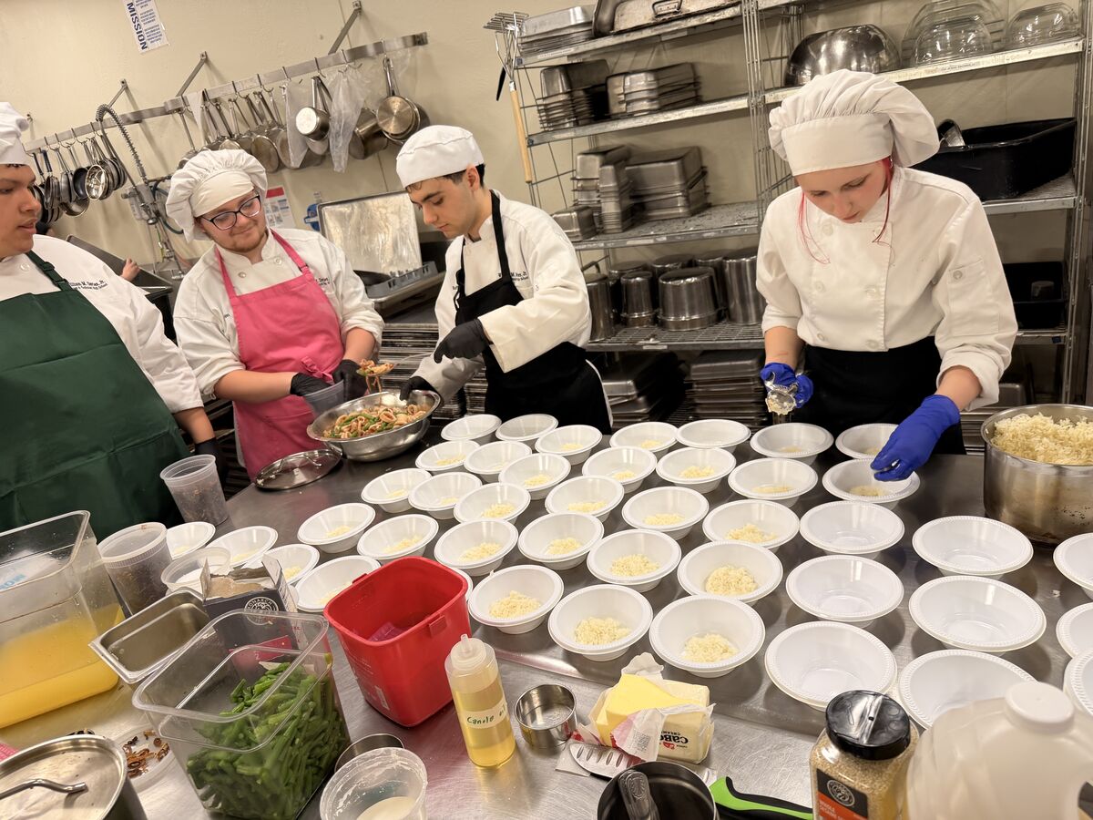 Davies culinary students in chef hats and aprons working at a kitchen station preparing sample bowls.