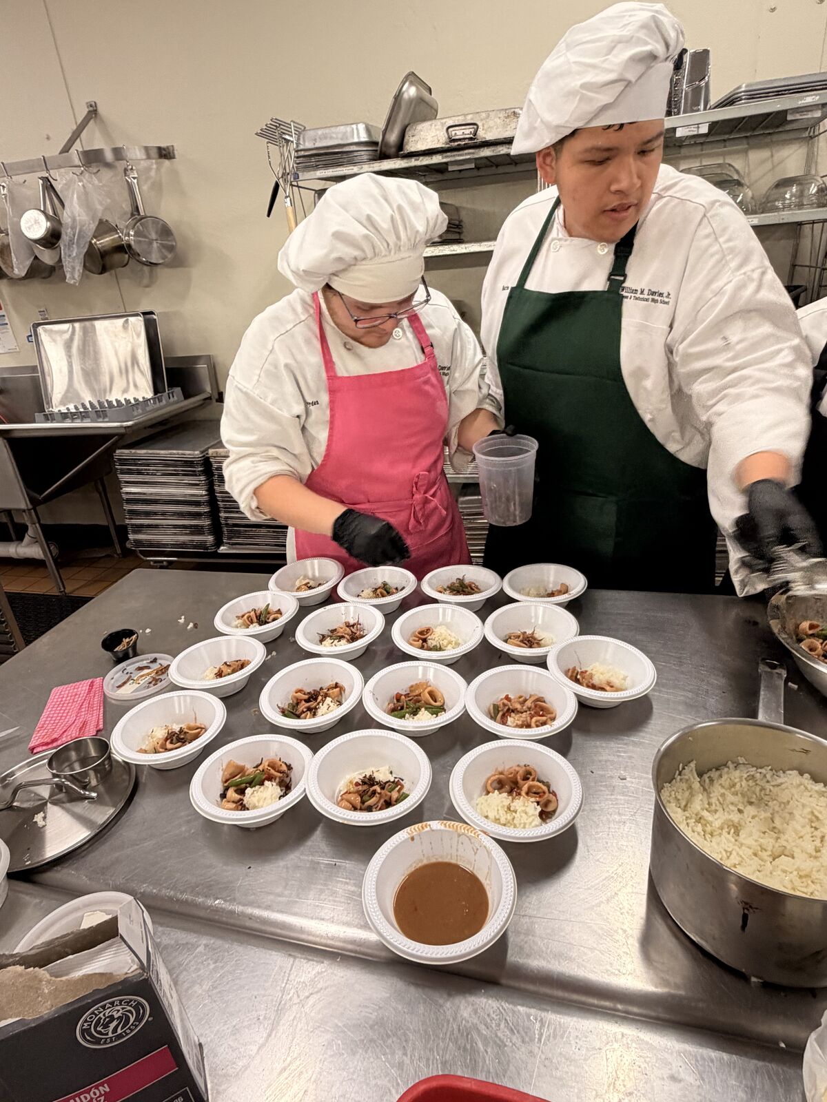Two students carefully plating individual servings in a commercial kitchen environment.