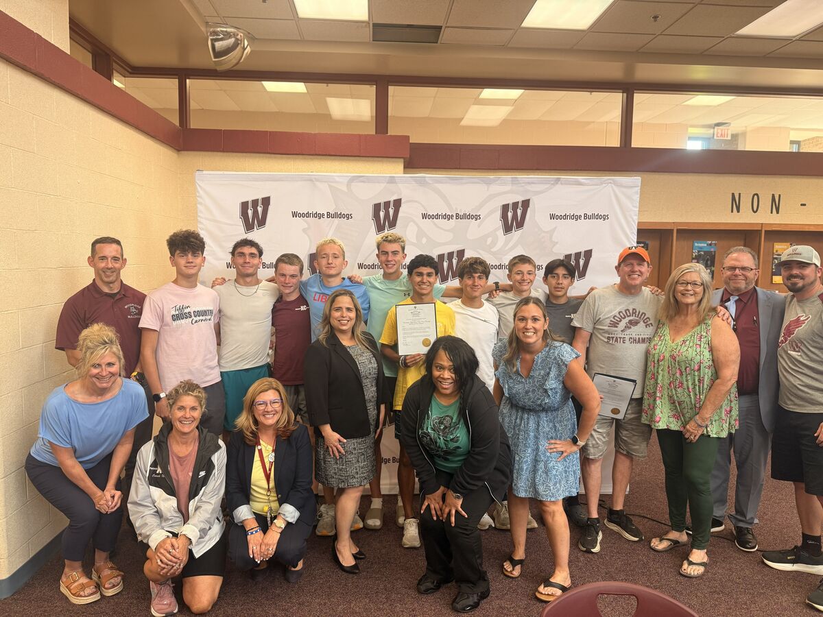 A group of students and adults pose for a photo in front of a banner that reads 'Woodridge Bulldogs'.