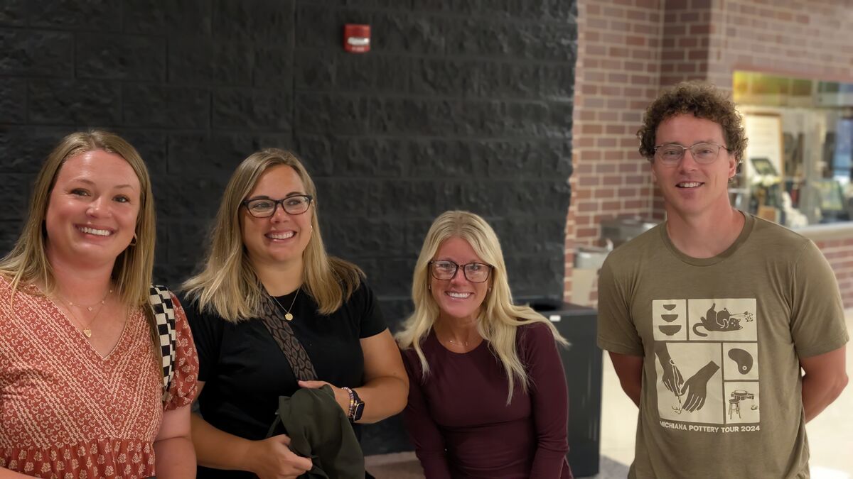 Four smiling people stand together in front of a dark brick wall and a brick column.
