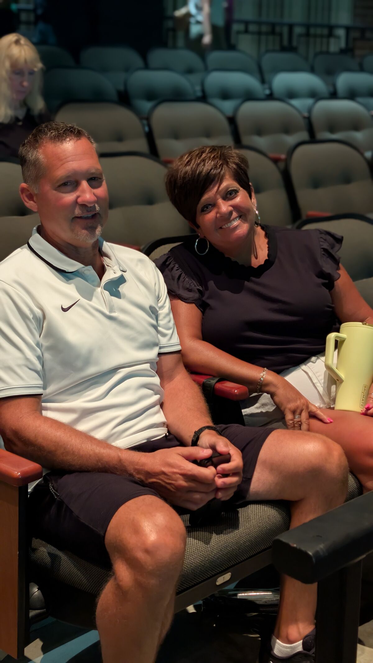 A smiling couple sits in theater seats, looking towards the camera.
