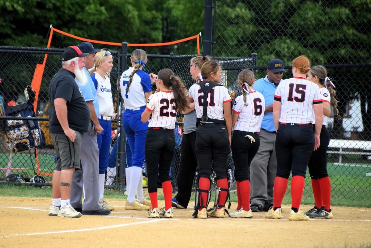 two teams on a softball field with umpires & coaches