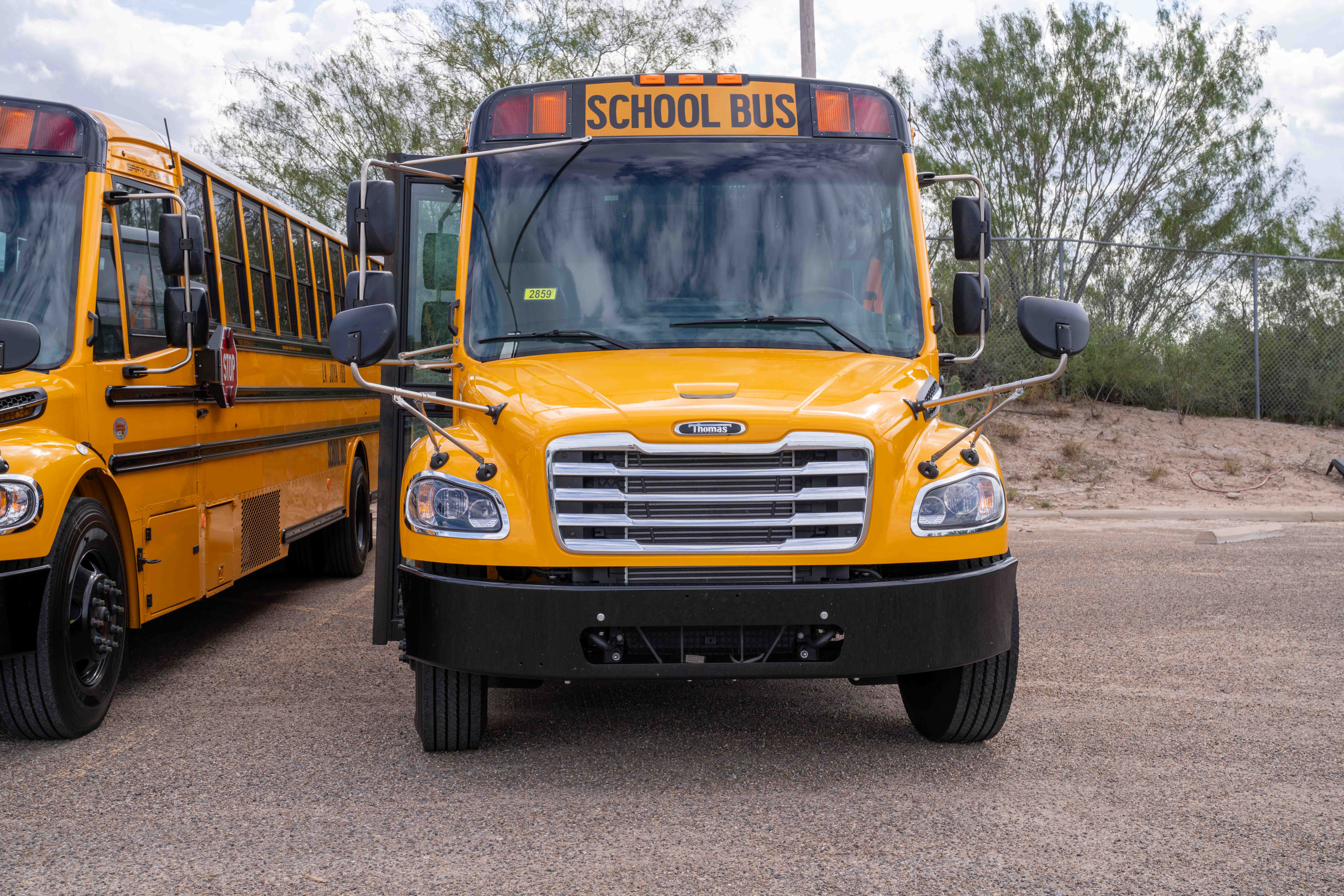 A bright yellow school bus parked outdoors, viewed from the front, with another bus partially visible on the left.