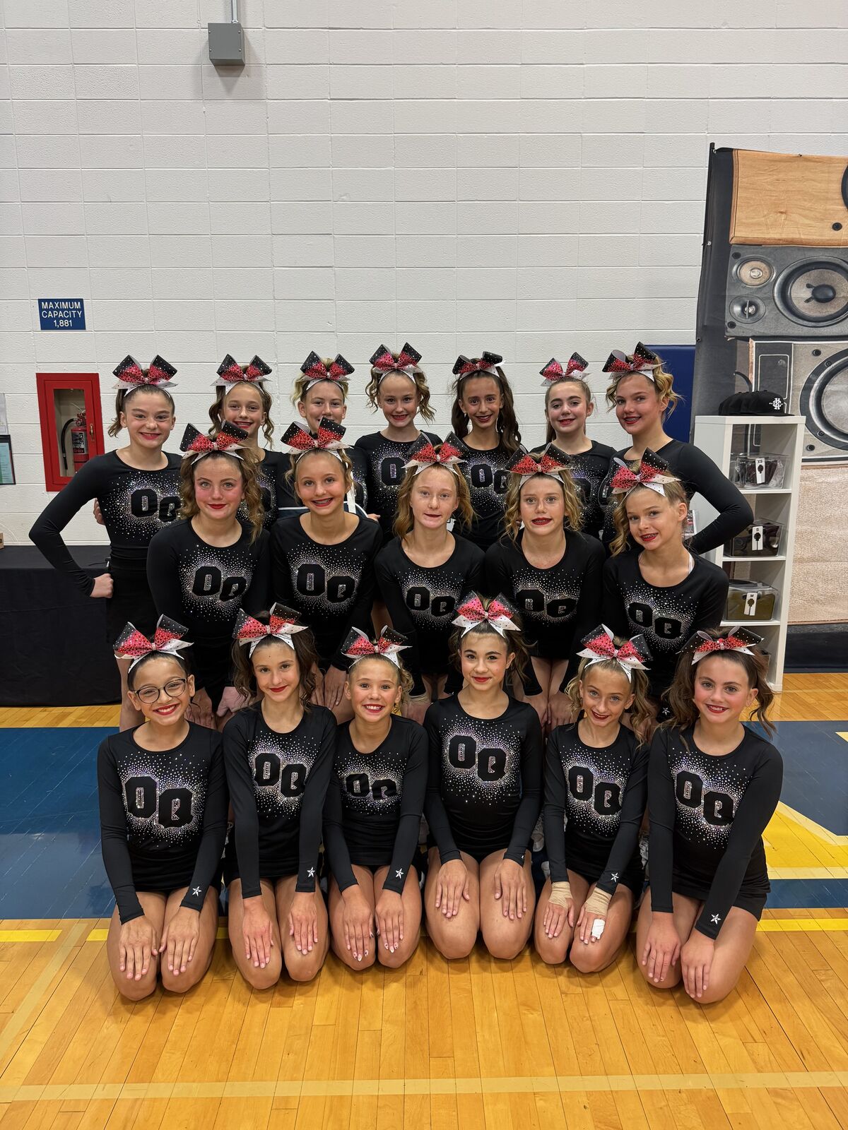 A group of young cheerleaders in matching black uniforms with sparkly 'OQ' logos pose for a photo.
