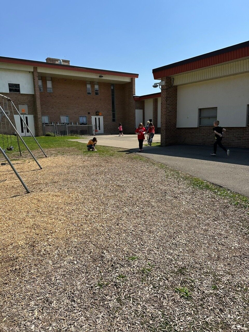 Children play on a school playground with swings and a paved area.