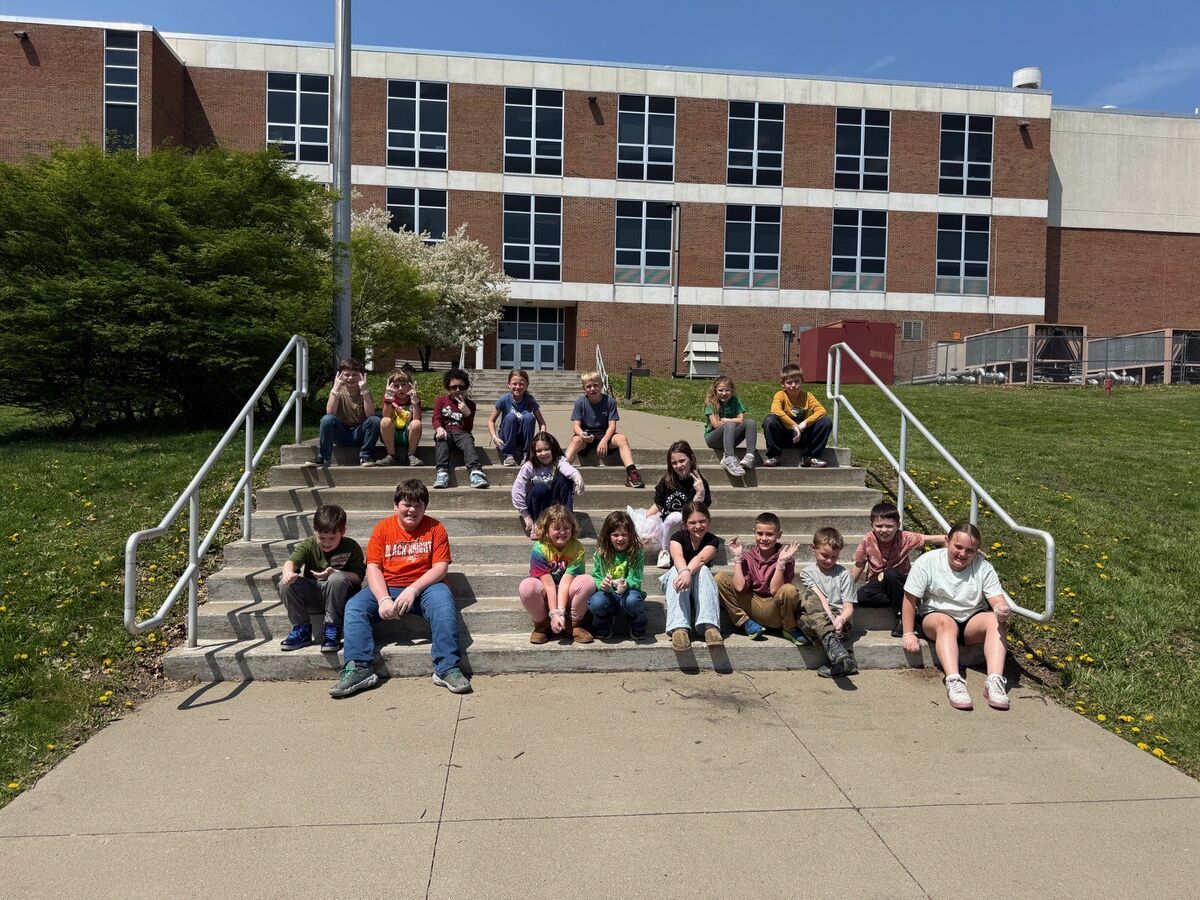 A group of children sit on school steps on a sunny day.