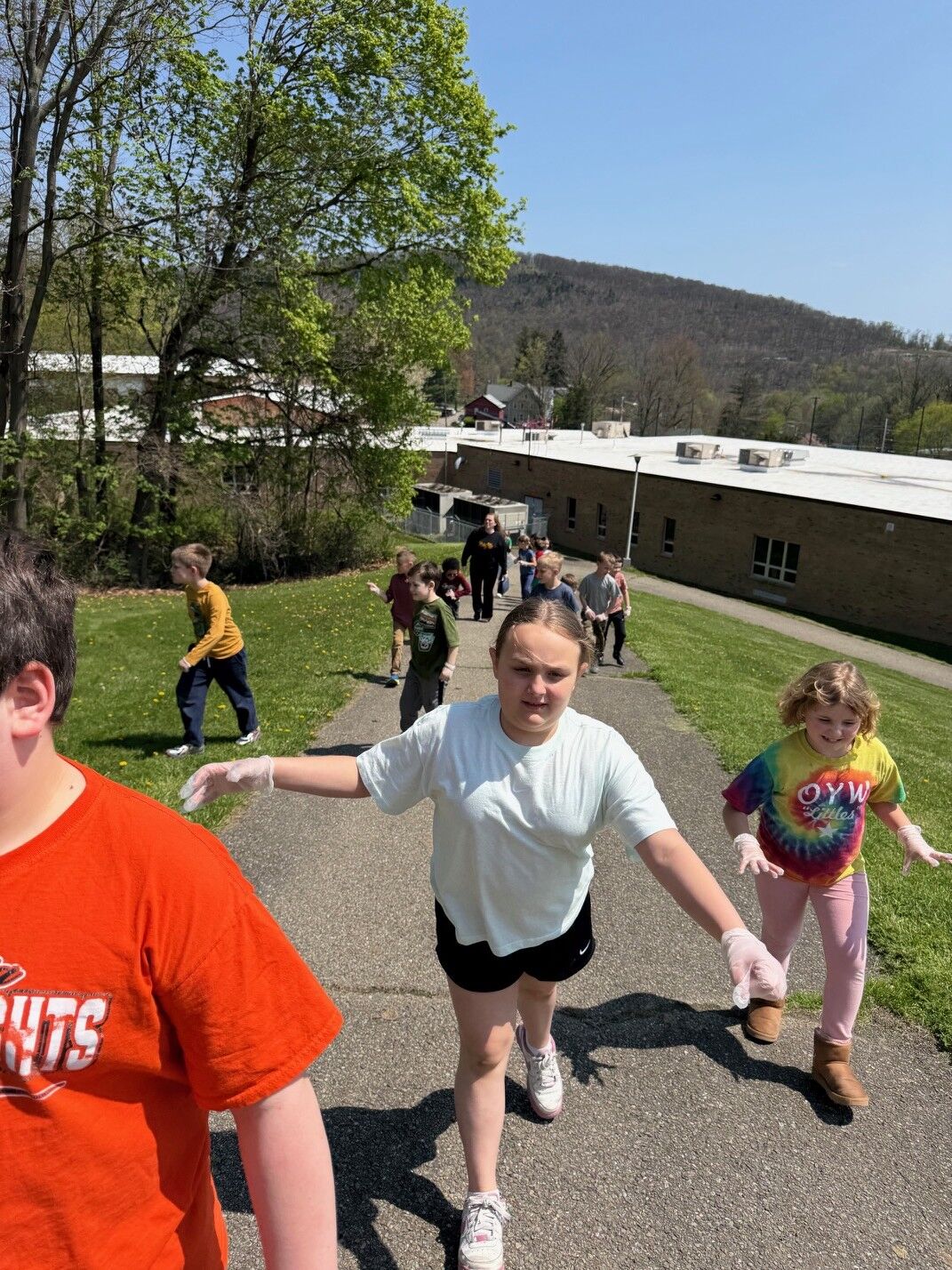 A group of children wearing gloves walk down a paved path outdoors.