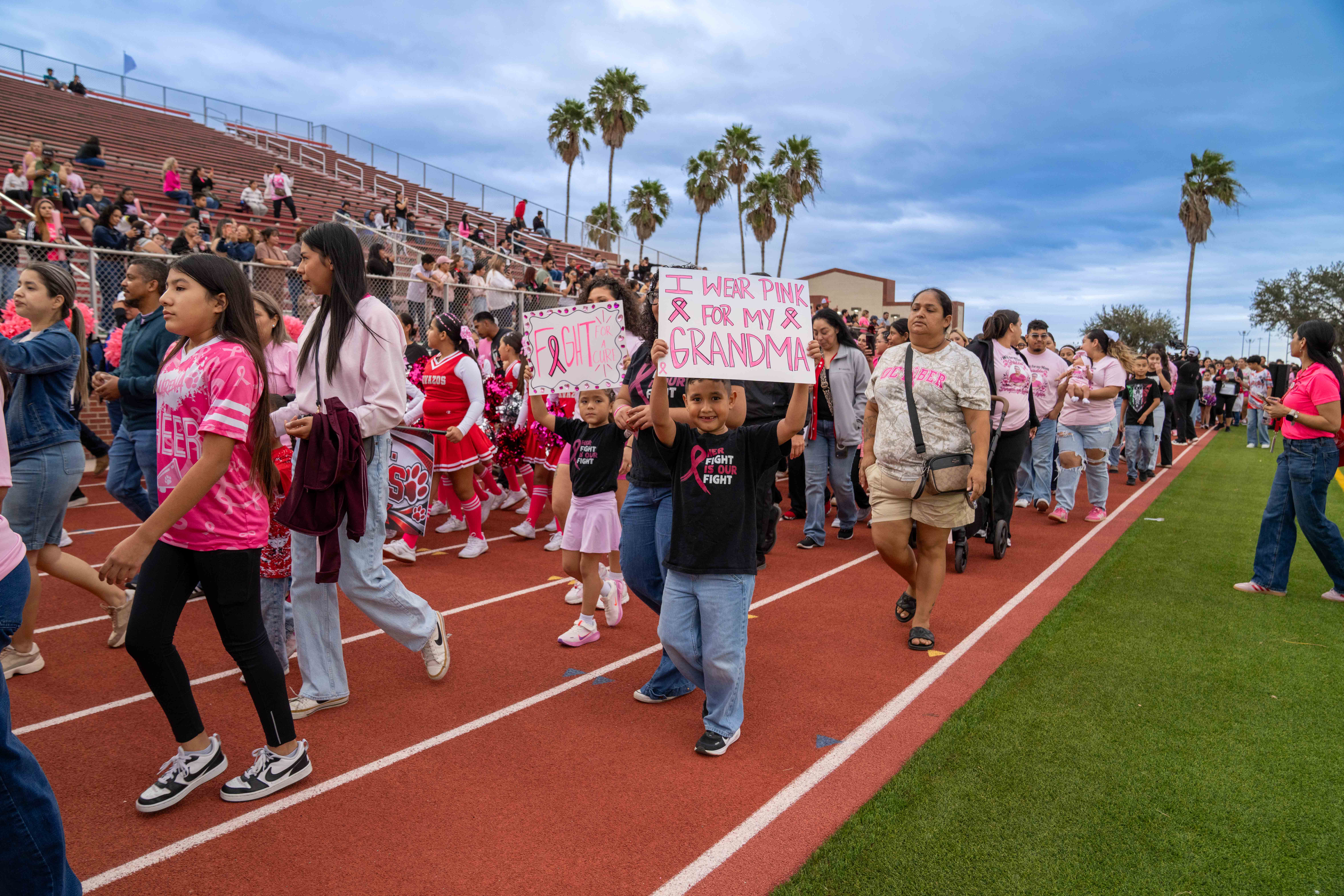 A group of people walk on a red running track at a stadium, participating in a breast cancer awareness event.