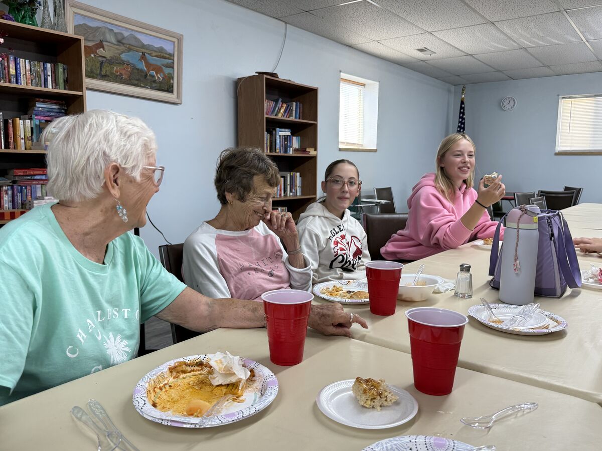 Four people of different ages sit at a table, sharing food and conversation.