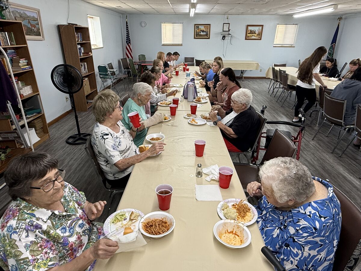 A group of people, including seniors and younger individuals, share a meal around a long table.