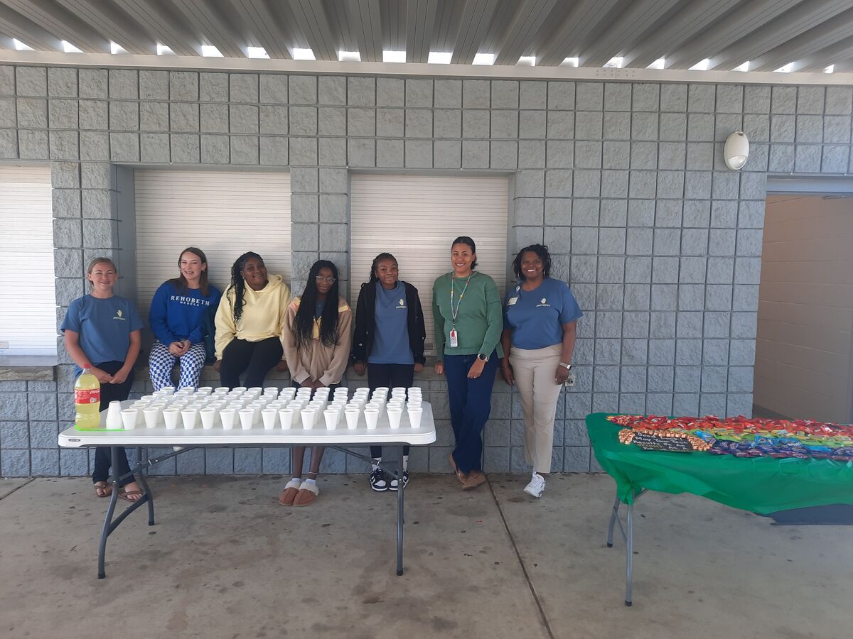 A group of young people and adults stand near tables set up with cups and snacks.