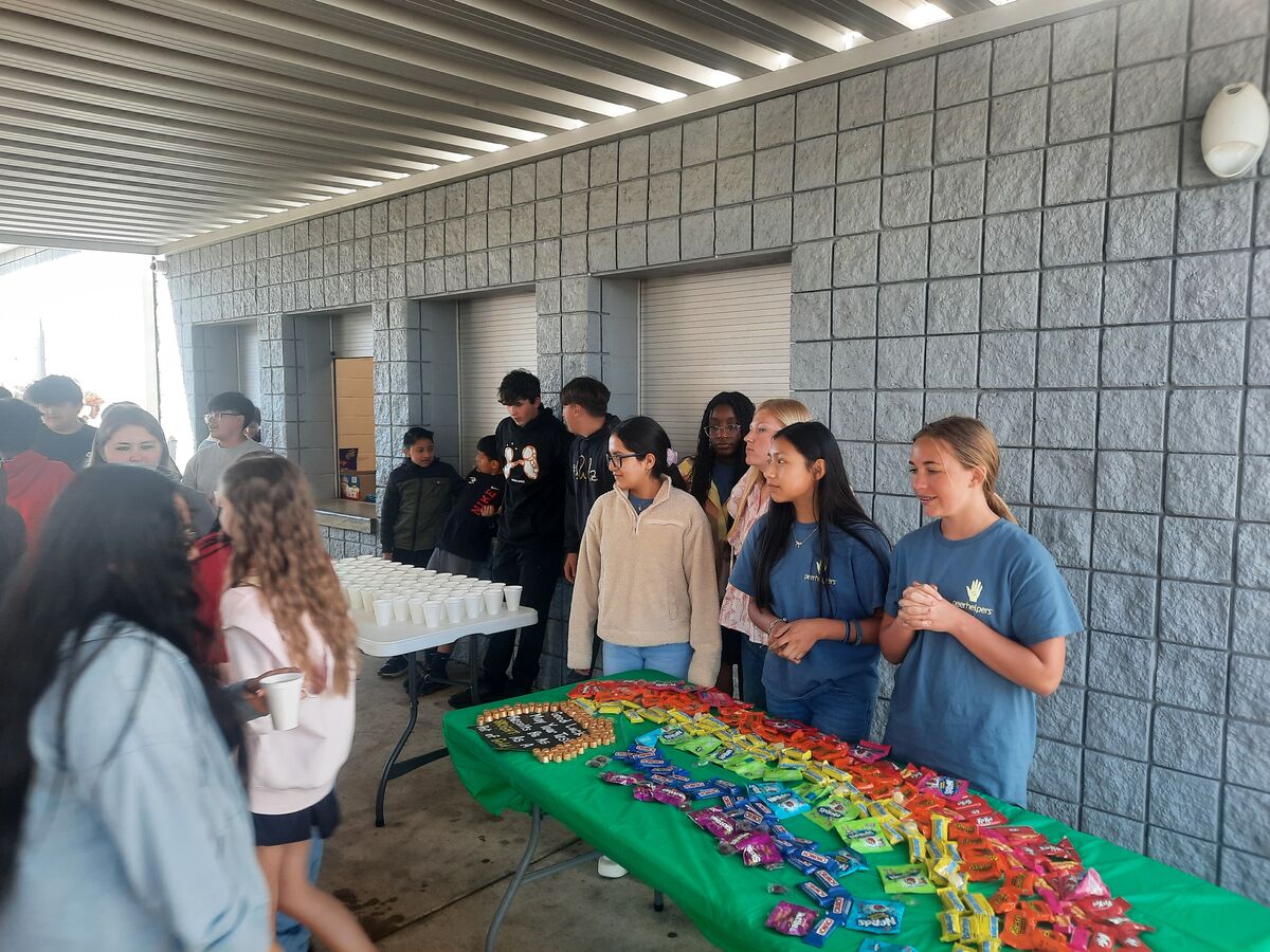 Students line up at tables with drinks and colorful candy arranged in a rainbow pattern.
