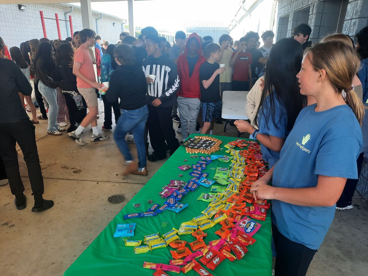 A group of students gathers around a table laden with colorful candy bars and snacks.