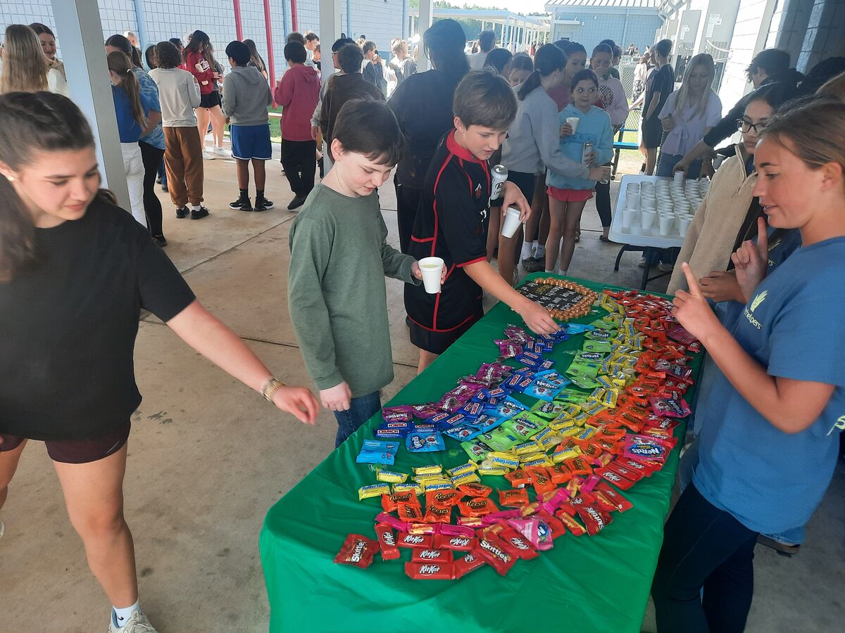 A group of students selects candy from a table covered with a green cloth, arranged in rainbow colors.