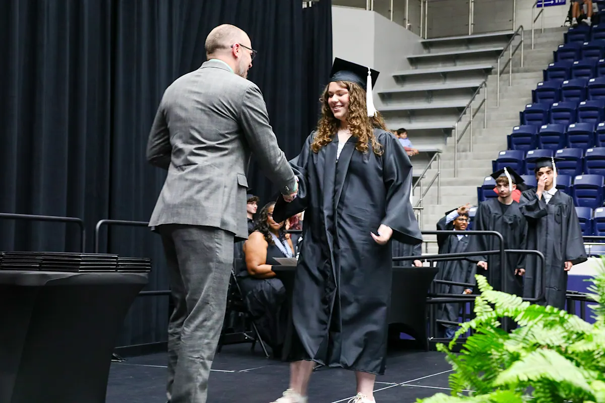 Achieve Academy graduate walking the stage and receiving her diploma from a board member.