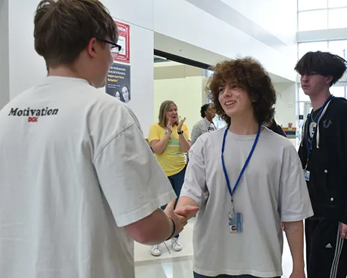 An Achieve Academy graduate shaking hands with another student in the hallway.