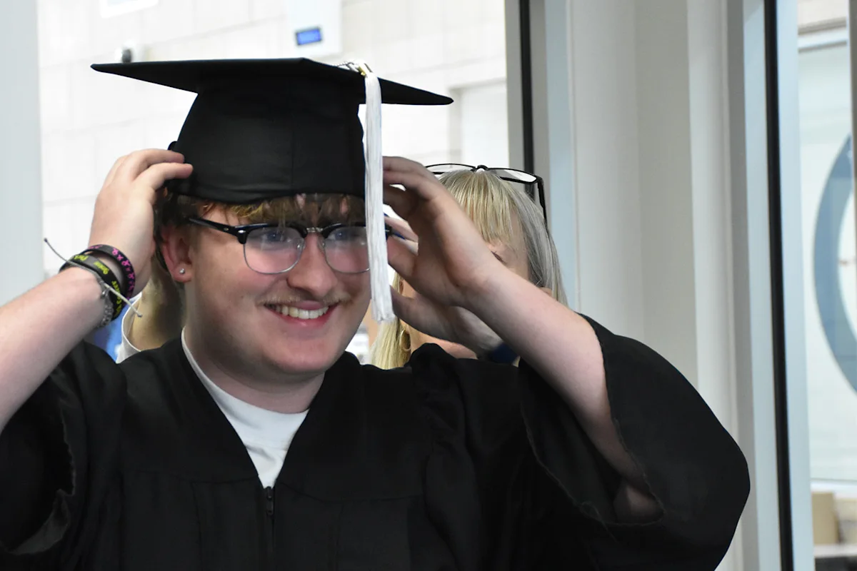 An Achieve Academy graduate smiling while he puts on his graduation cap.