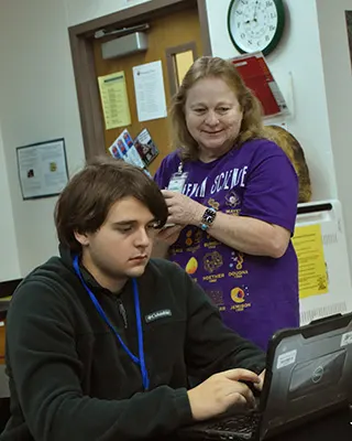 An Achieve Academy student working on a laptop while his teacher looks on.
