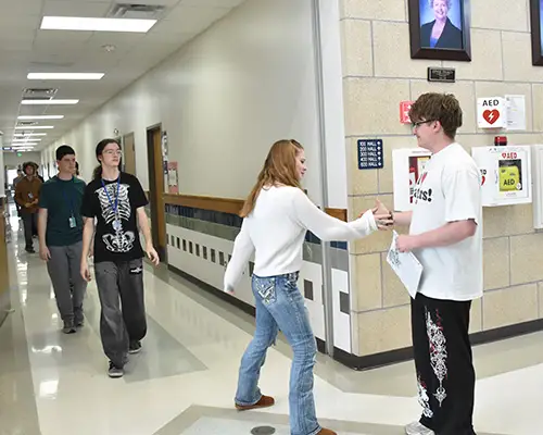 An Achieve Academy graduate shaking hands with another student in the hallway.