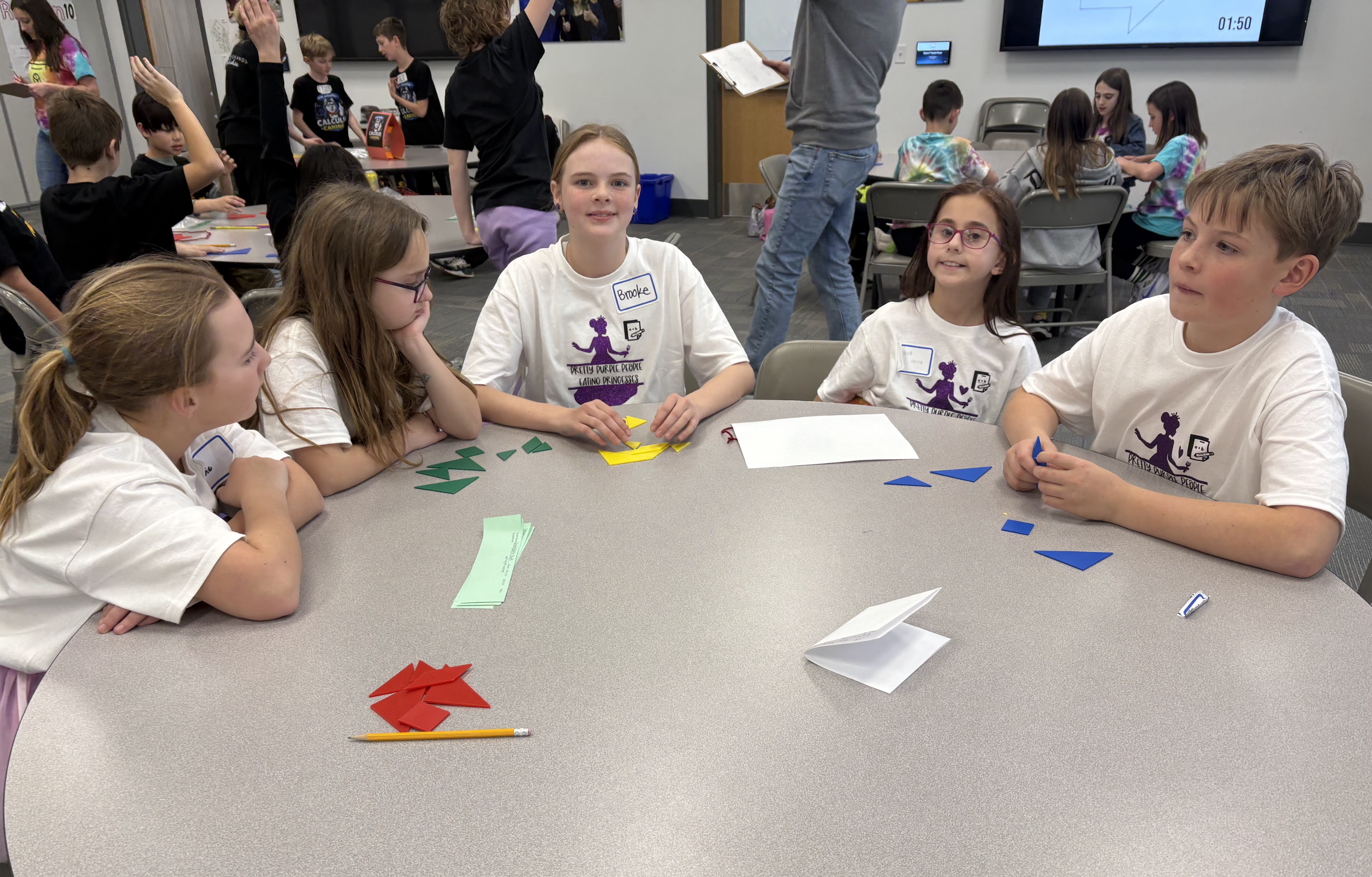 Children sit at a table, engaged in a hands-on activity with colorful geometric shapes.