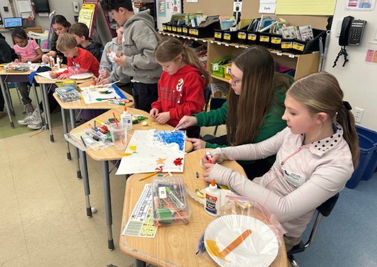 Students engaged in an art project at their desks, surrounded by craft supplies.
