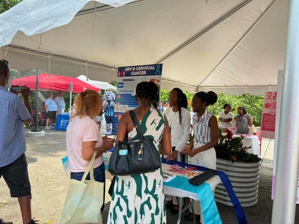 People gather under a white tent at an outdoor event, with informational posters.