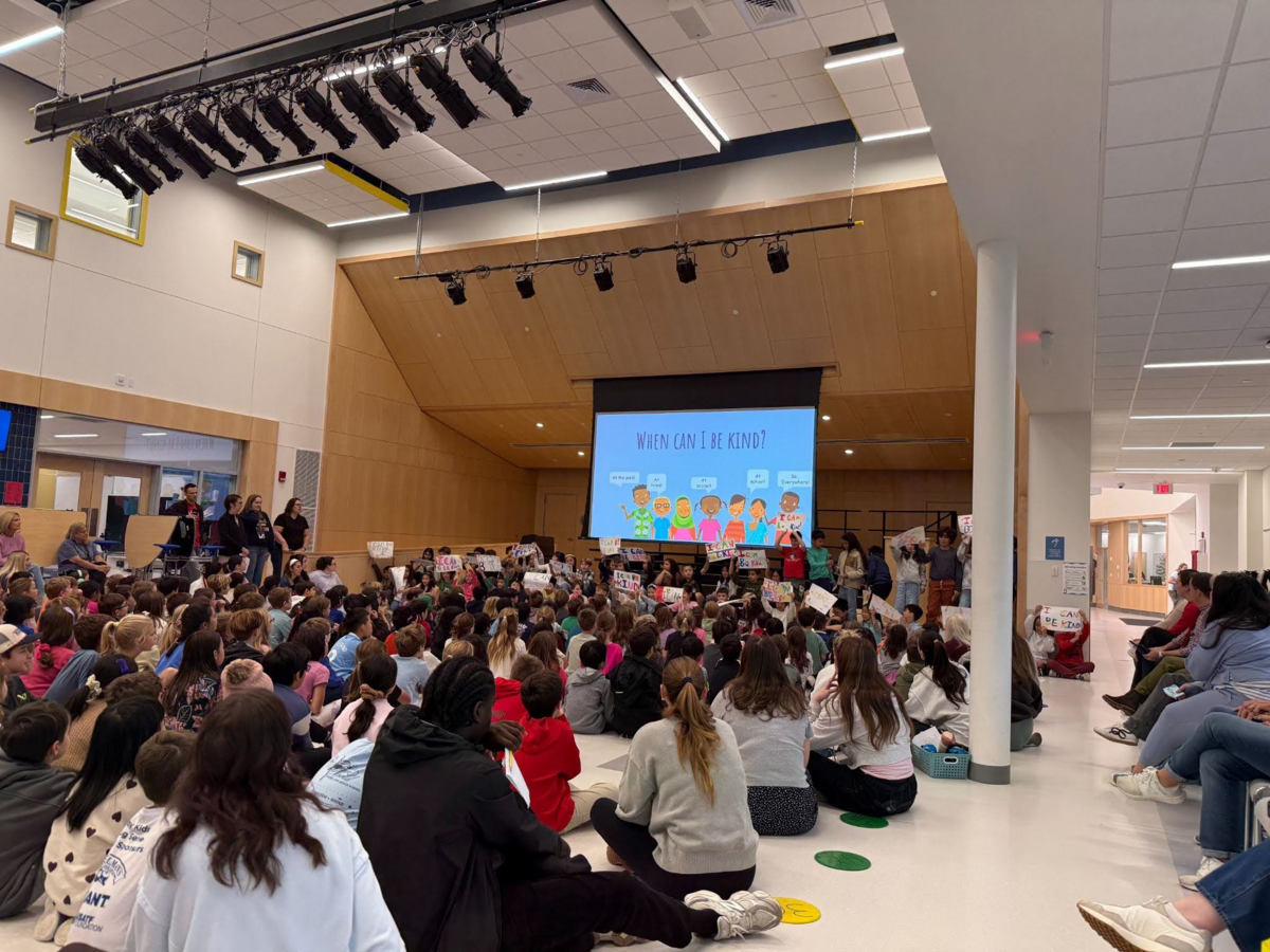 Students watch a presentation at a school assembly from the 4th graders. A slide on the screen reads 