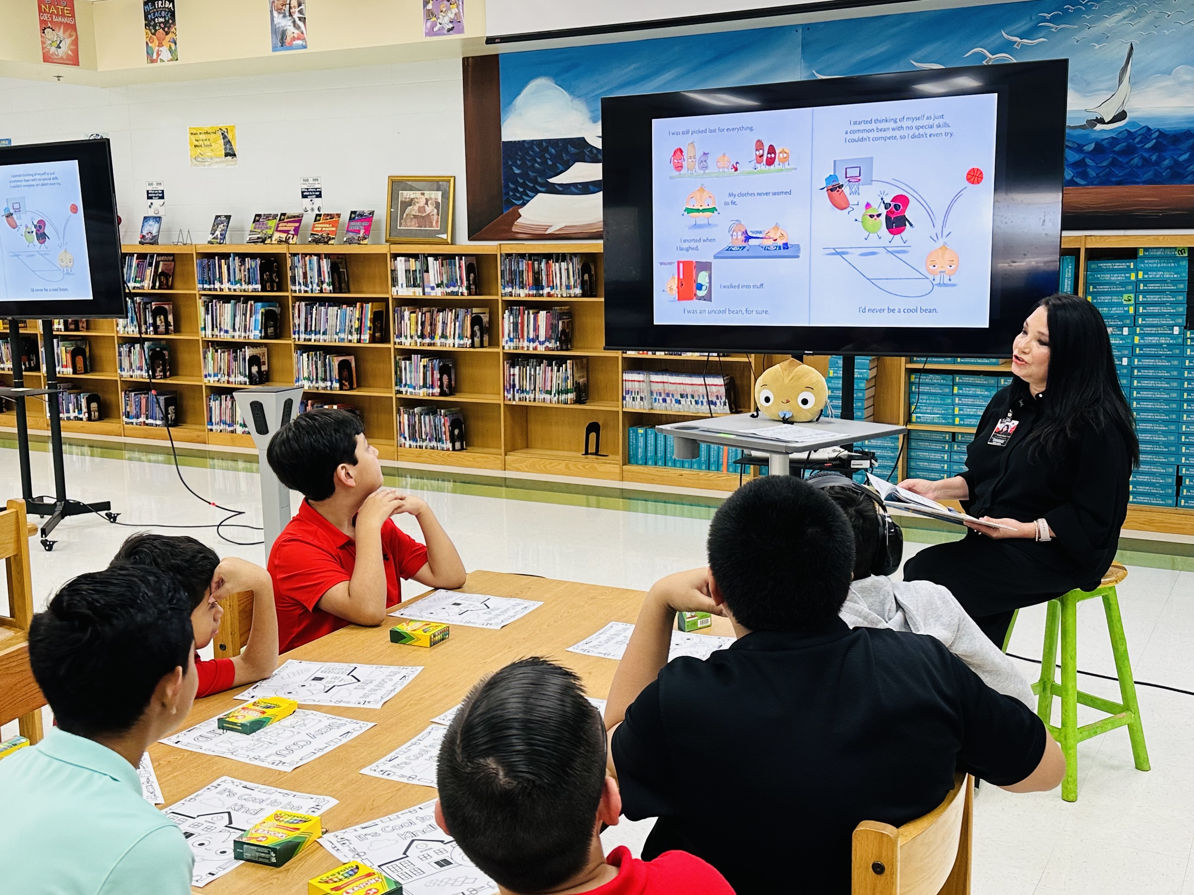 A teacher reads a story to a group of attentive children in a library.