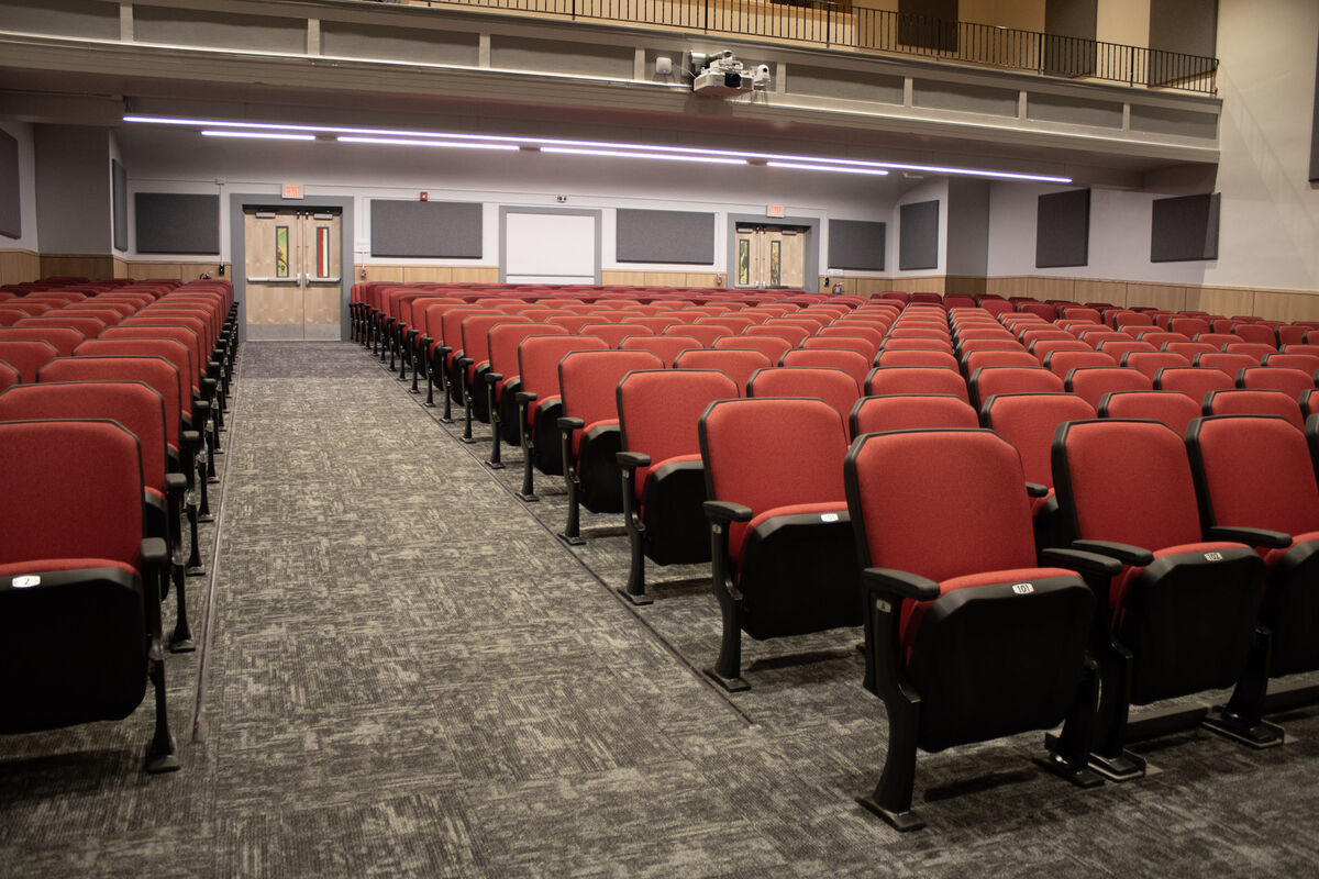 Rows of empty red theater seats with black accents are arranged in an auditorium.