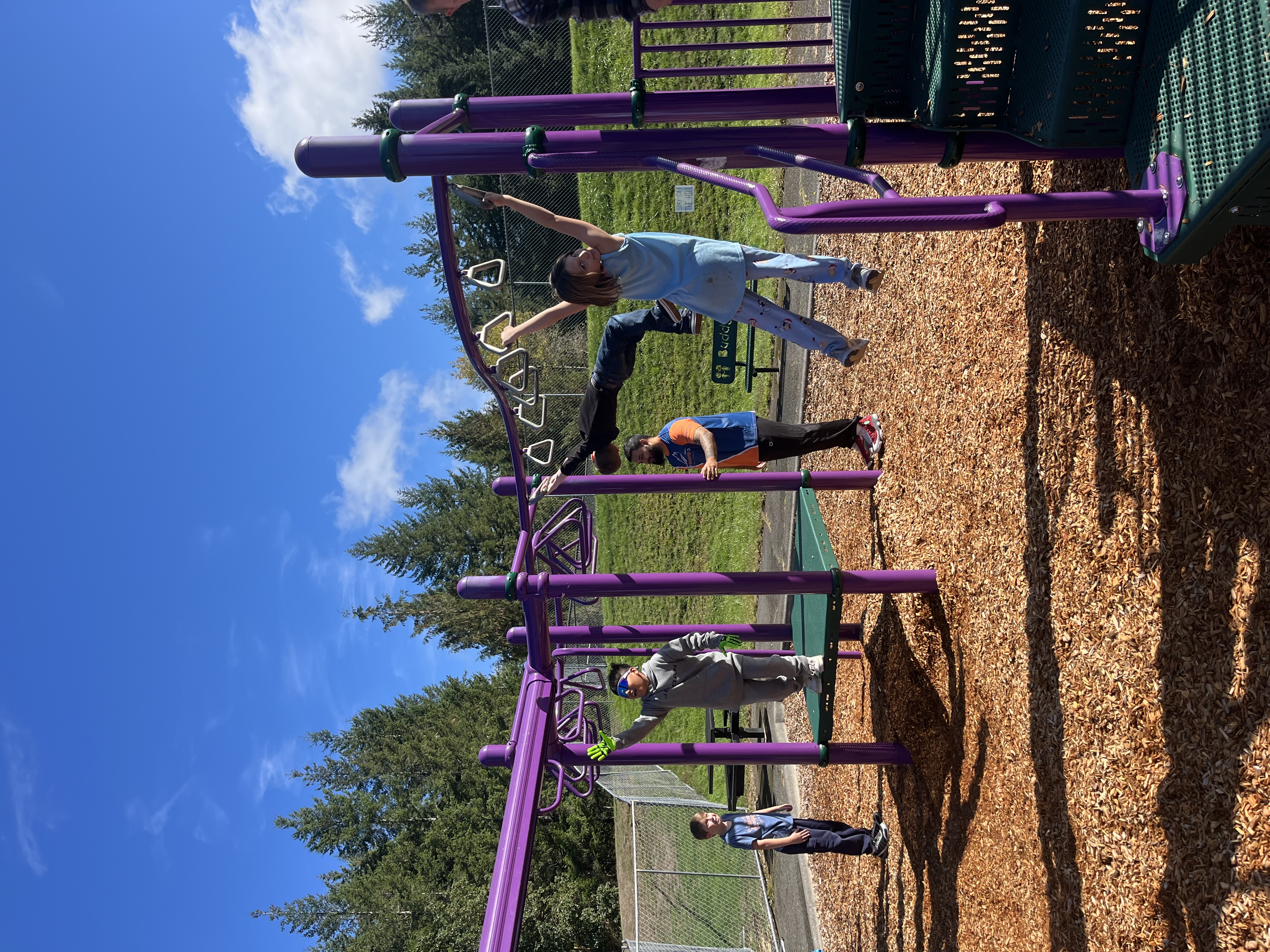 A group of people enjoy a sunny day climbing and playing on a purple playground structure.