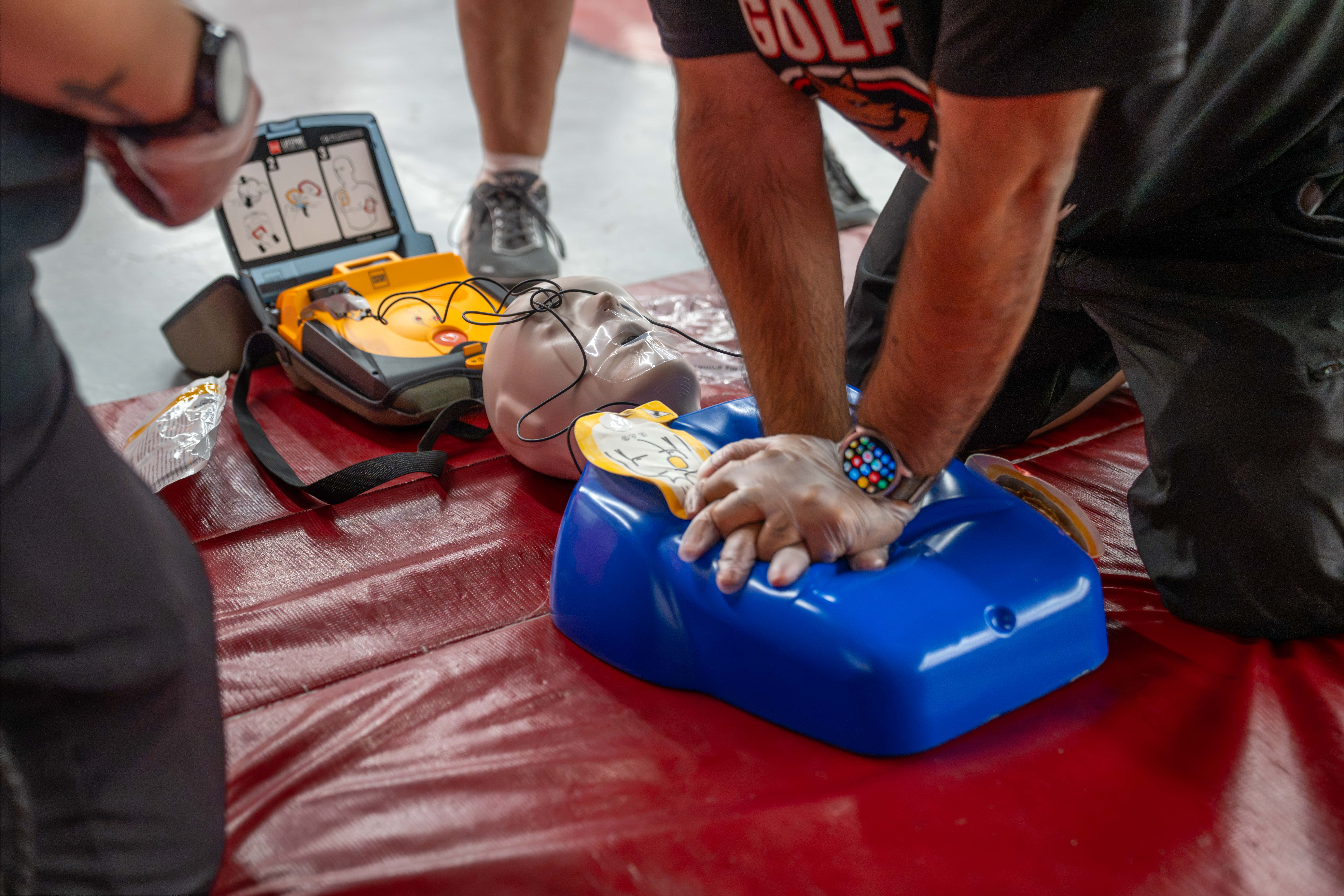 A person practices CPR on a training dummy with an AED device nearby.