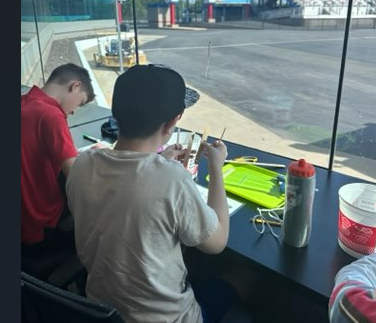Two boys are engaged in a craft activity at a table with a view of an outdoor area.