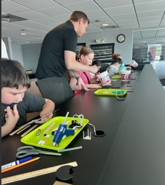 A group of children and an adult are engaged in a craft activity at a long table.