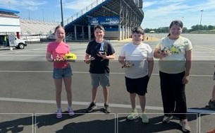 Four children stand in a line outdoors, each holding a small object they've made.
