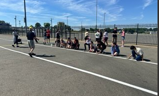A group of young people are painting white lines on an asphalt surface, guided by an adult.