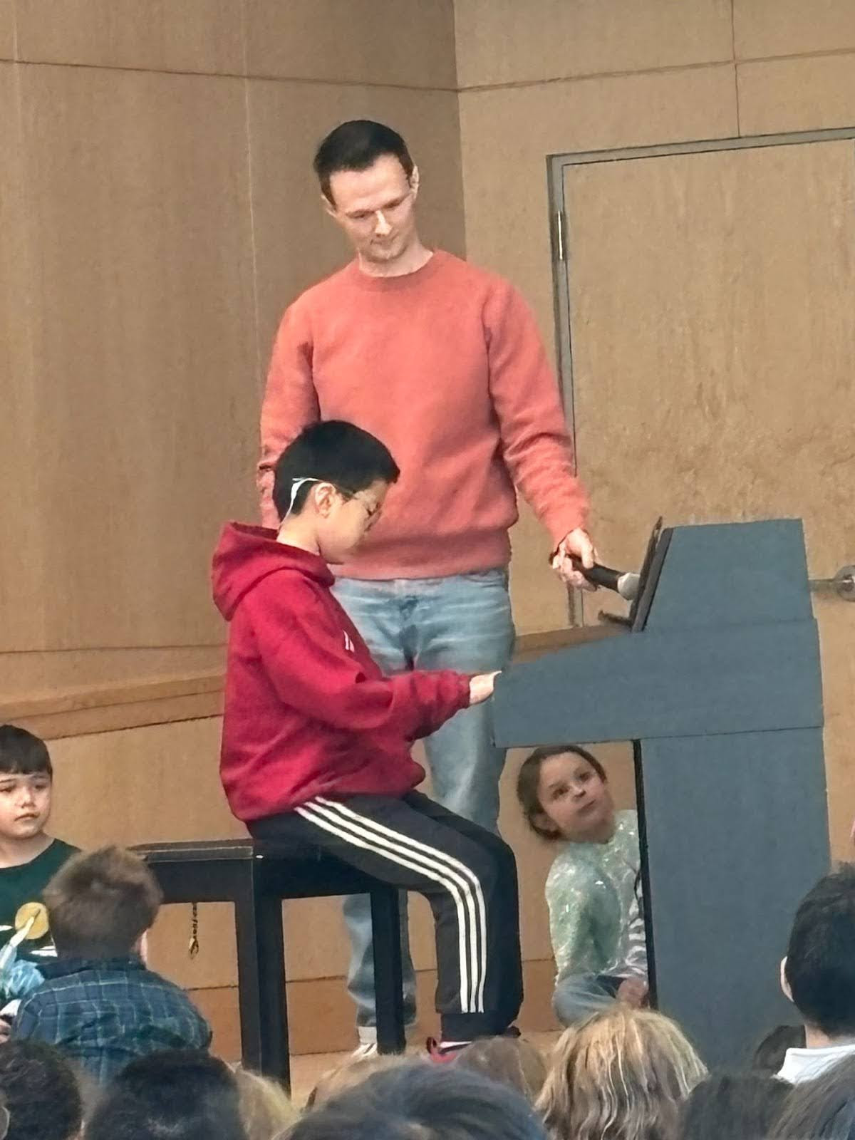 Mr. Corcoran holds microphone to piano while student plays during assembly. 