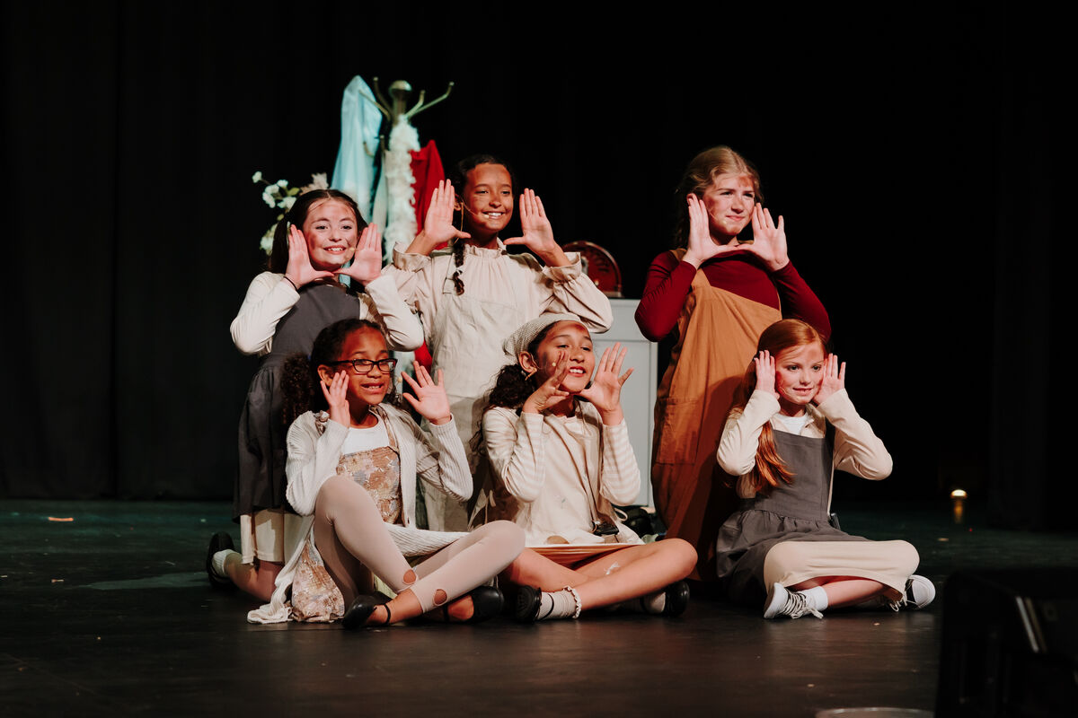 6 children sitting and smiling on stage for a performance