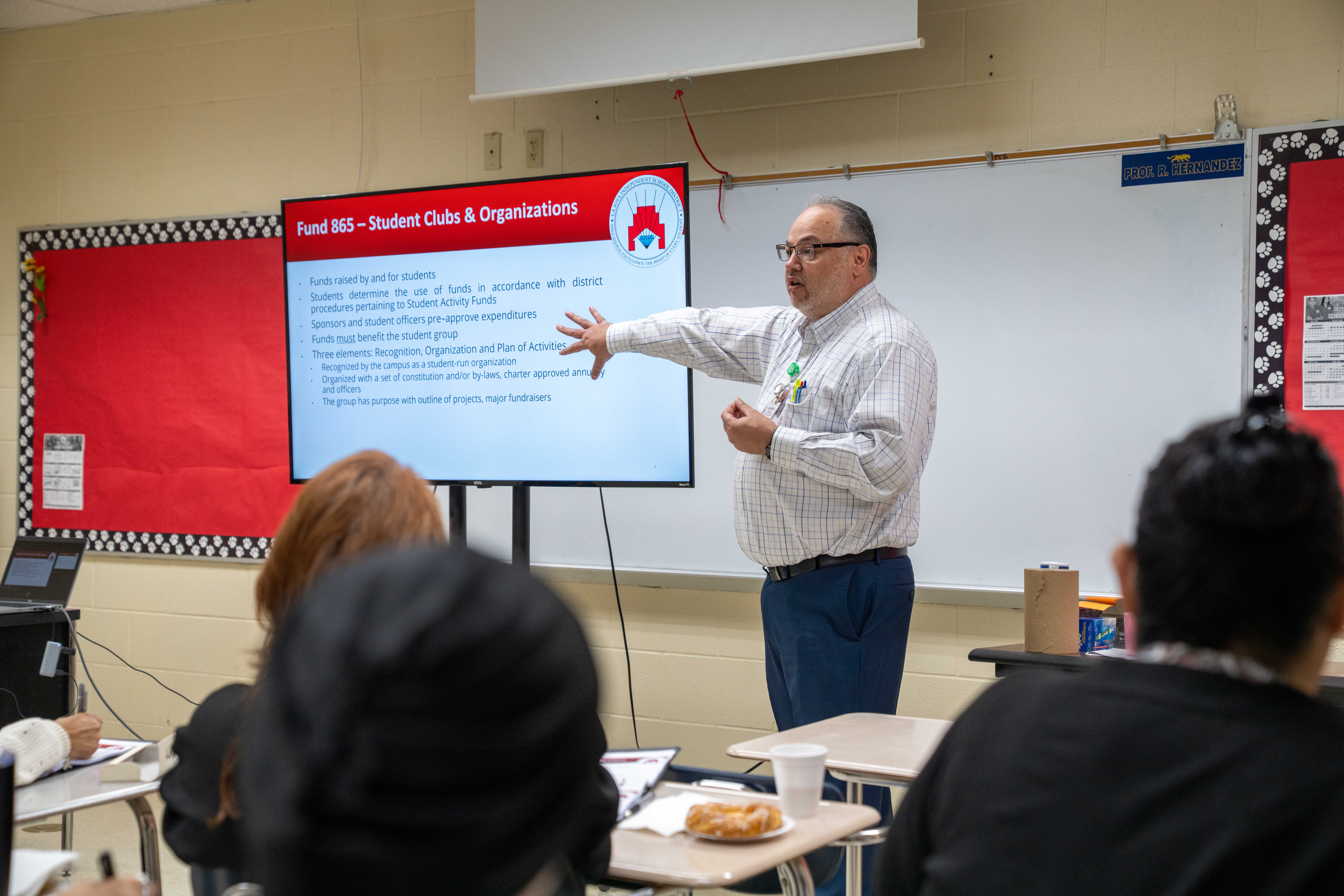 A presenter points to a screen displaying information about "Fund 865 - Student Clubs & Organizations" in a classroom.