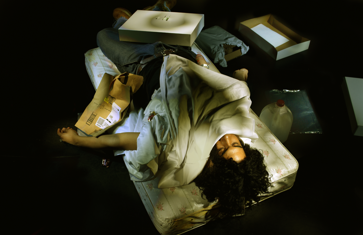 A person rests on a mattress surrounded by various boxes and packaging.