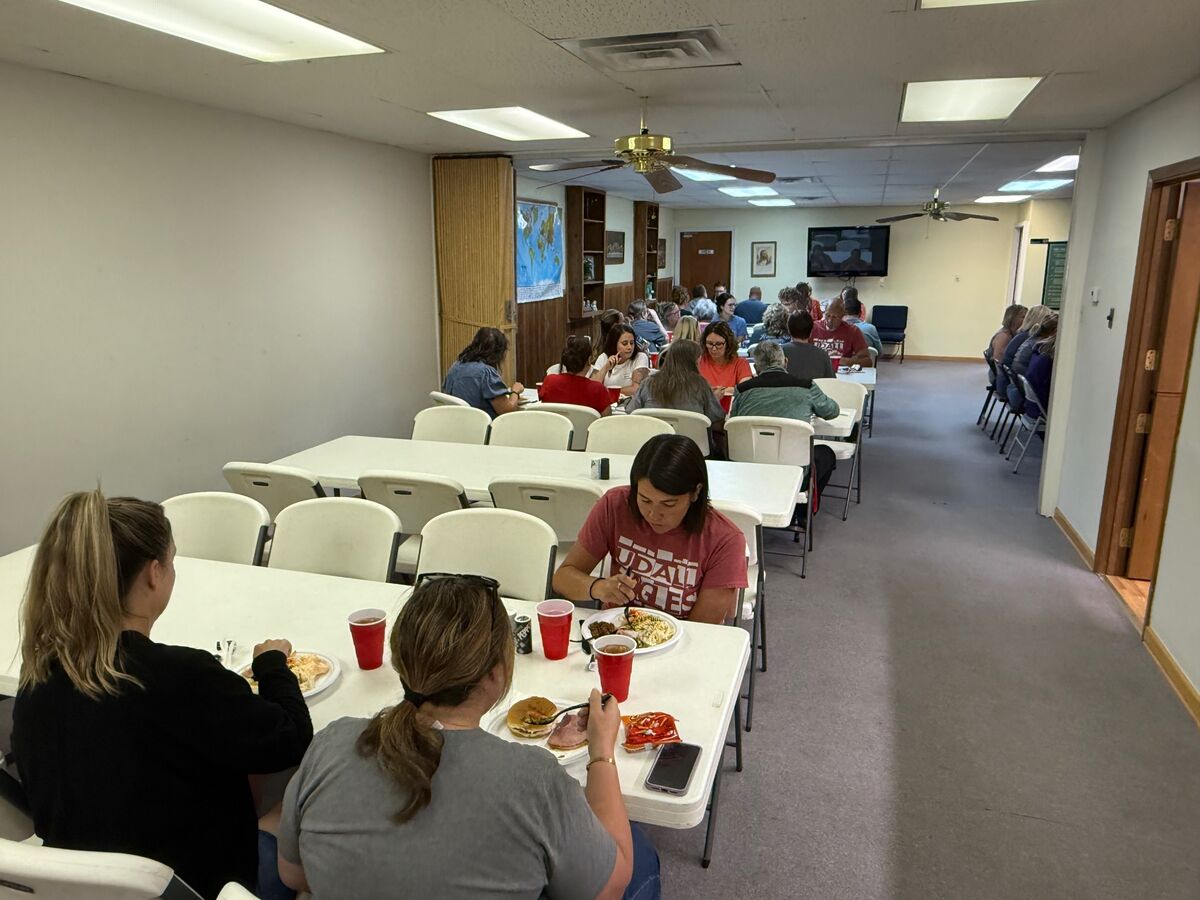 A group of people are seated at long tables, eating meals and conversing.