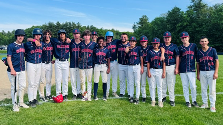 A baseball team poses for a photo on a grassy field, wearing matching navy and red uniforms.