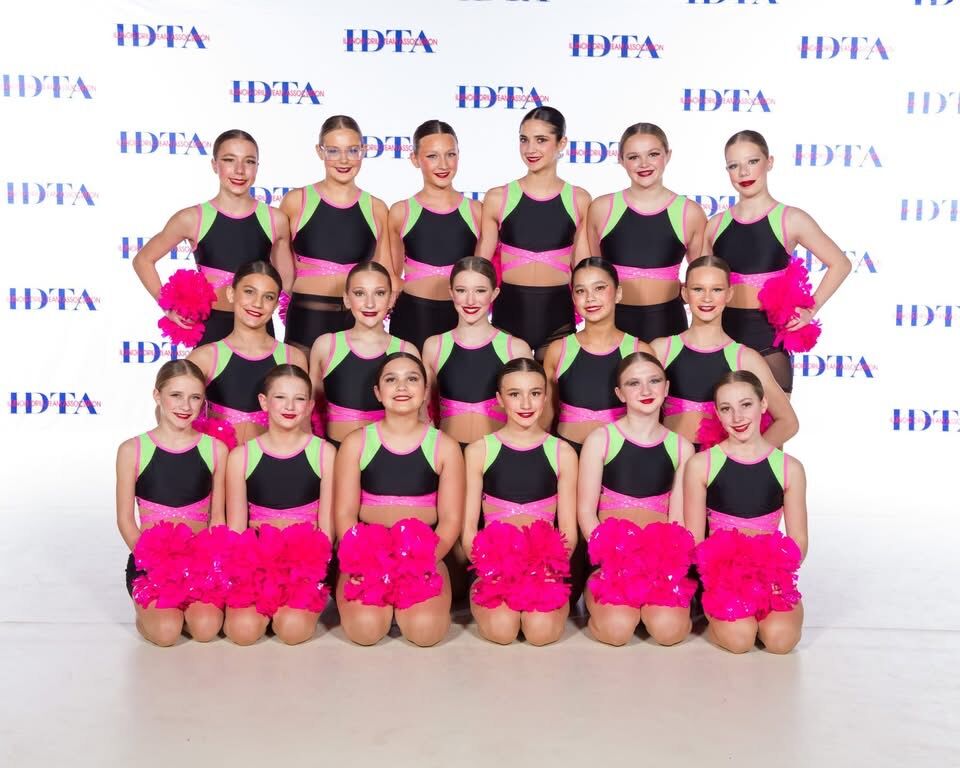 A dance team poses for a photo in matching black and neon green outfits with pink pom-poms.