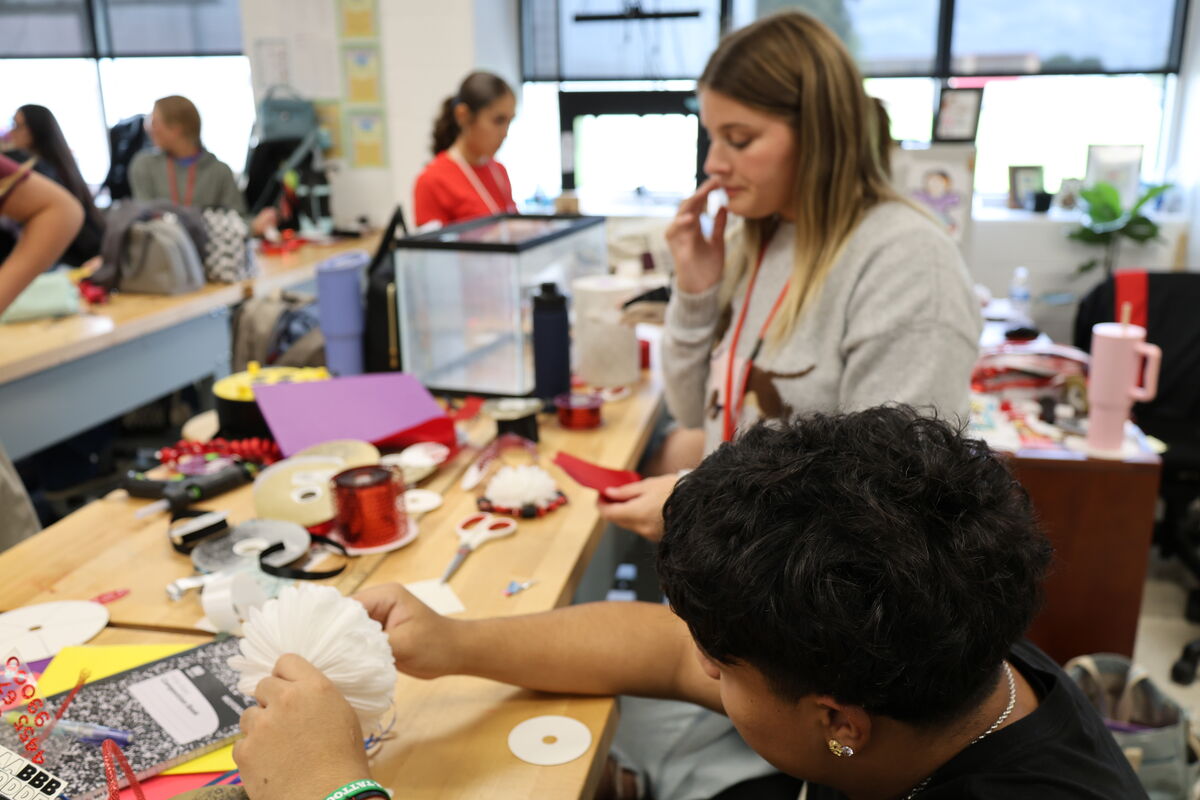 Students work on craft projects at wooden tables in a bright classroom.