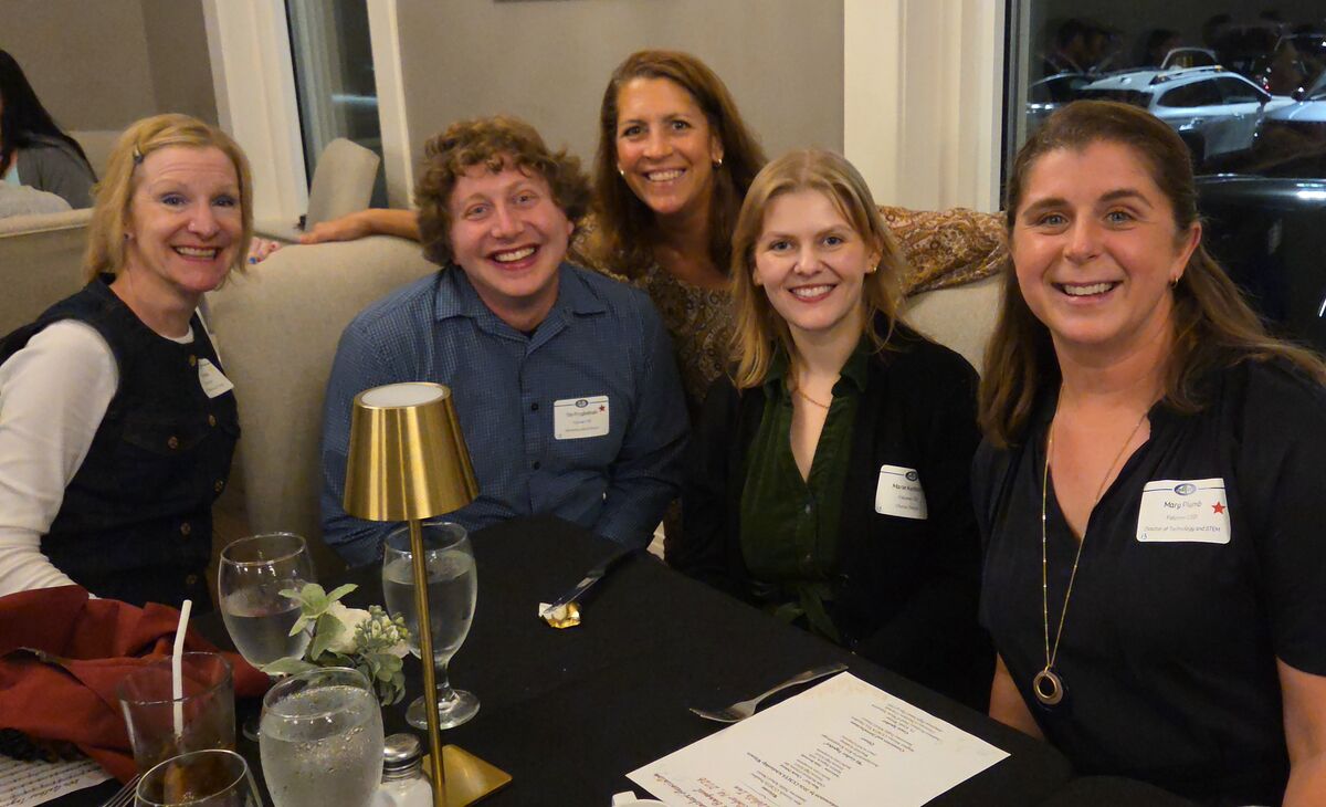 Five smiling people sit together around a dark dining table with name tags.