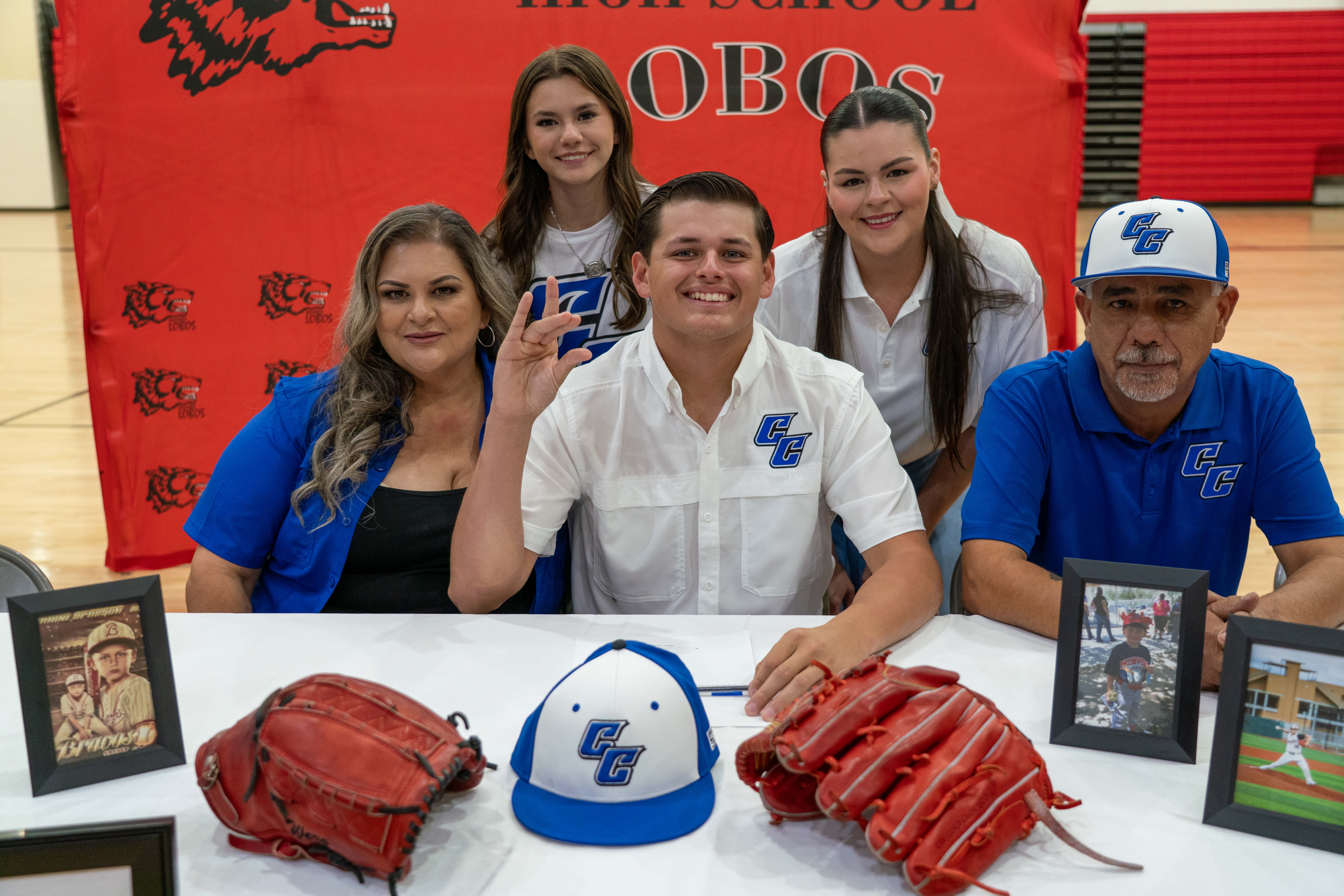 A family poses for a photo behind a table with baseball equipment and framed pictures.