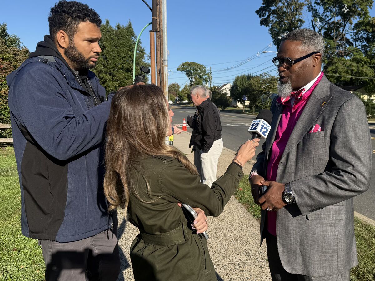 A news reporter holds a microphone interviewing a man in a gray suit
