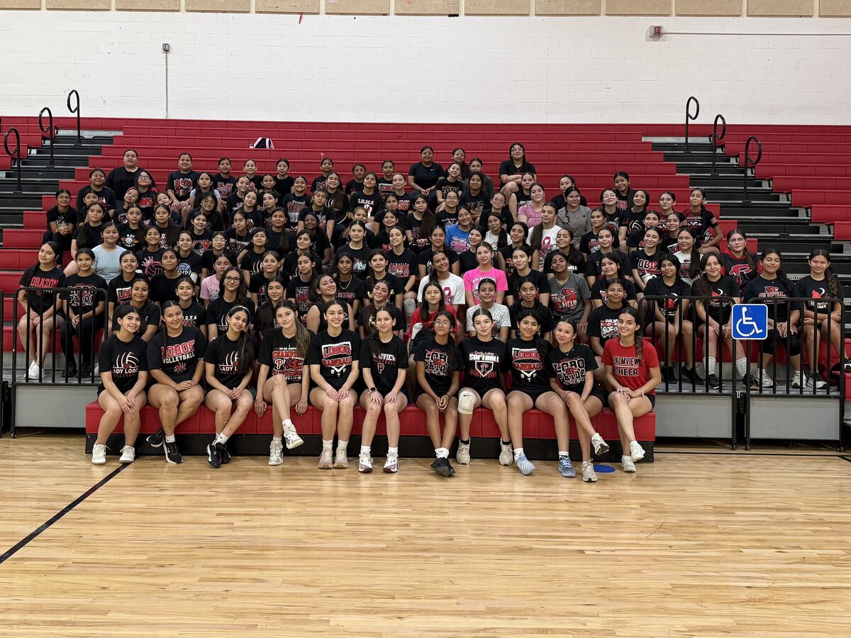 A large group of young women in athletic wear pose for a photo on bleachers in a gymnasium.