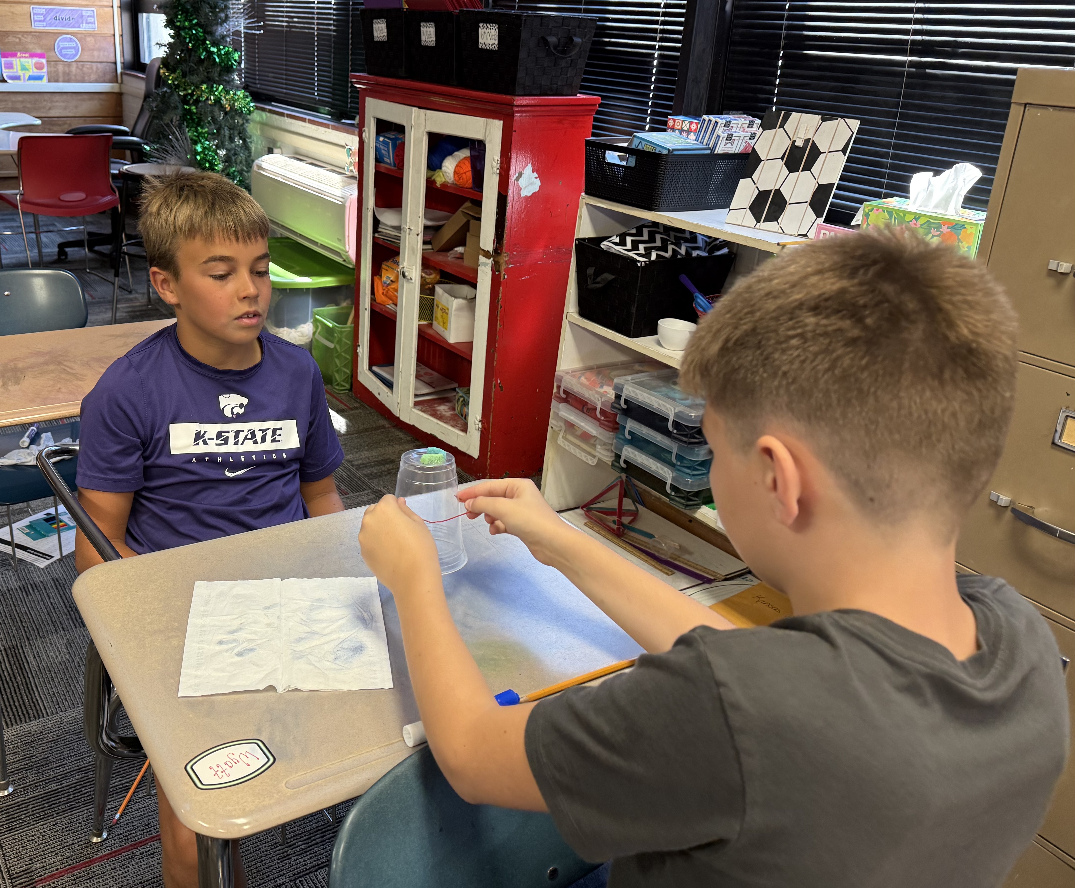 Two boys are engaged in a science experiment at their desks in a classroom.
