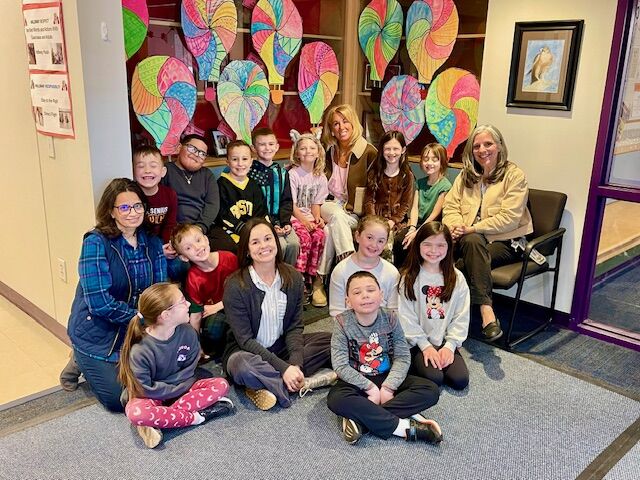 A group of children and adults pose for a photo in front of colorful hot air balloon artwork.