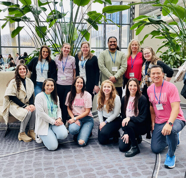 people stand in a casual indoor setting, smiling. 
